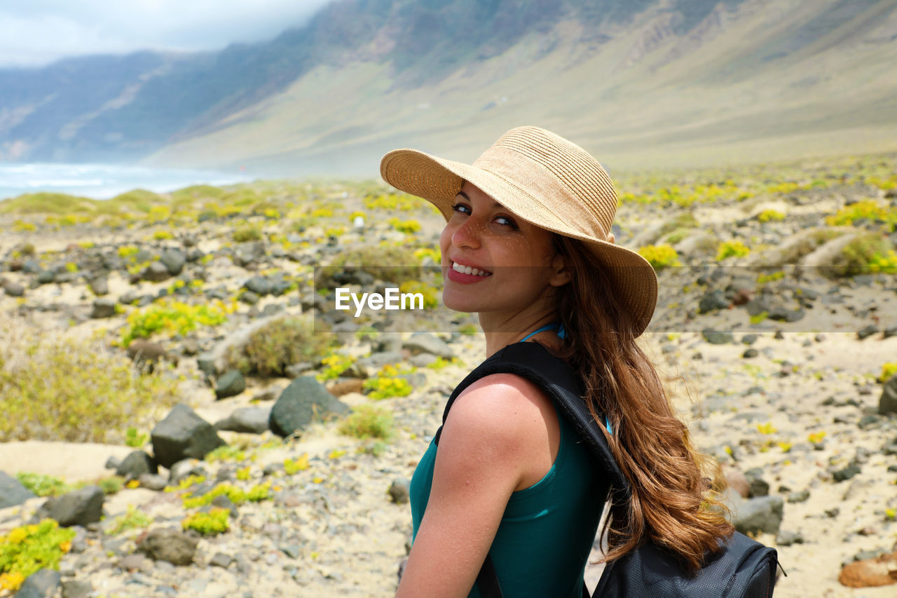 PORTRAIT OF BEAUTIFUL WOMAN WEARING HAT AGAINST MOUNTAINS