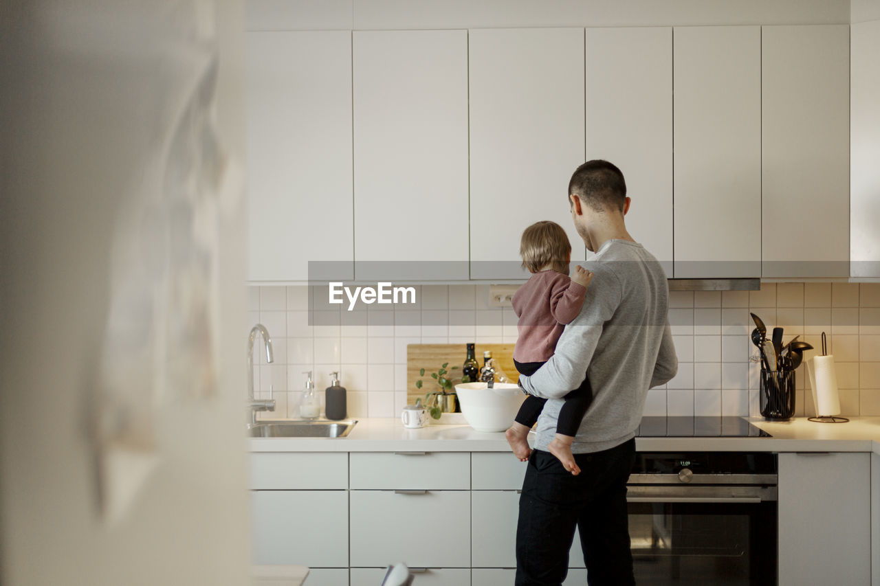 Father carrying toddler girl in kitchen
