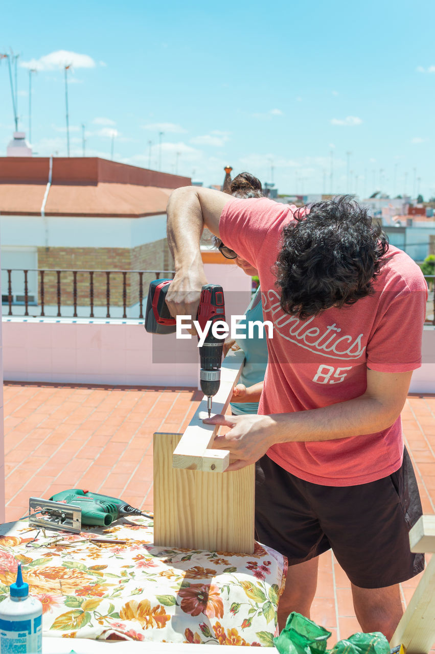 Couple building a piece of furniture on a rooftop on a sunny day.