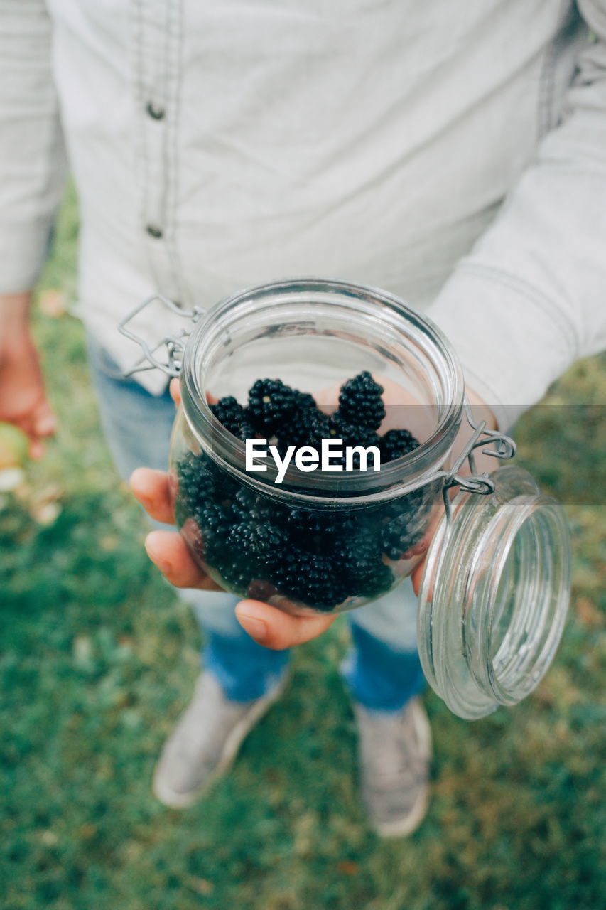 Low section of man holding blackberries in jar on field