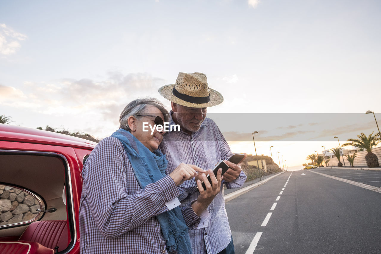 Senior couple using smart phone while standing on road against sky