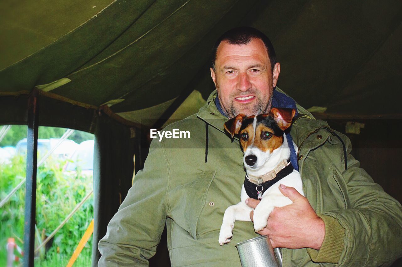 Portrait of smiling man with jack russell terrier standing in tent at campsite