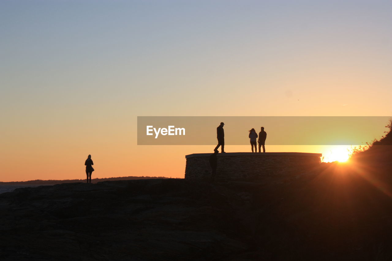 Silhouette people walking on sand against clear sky during sunset