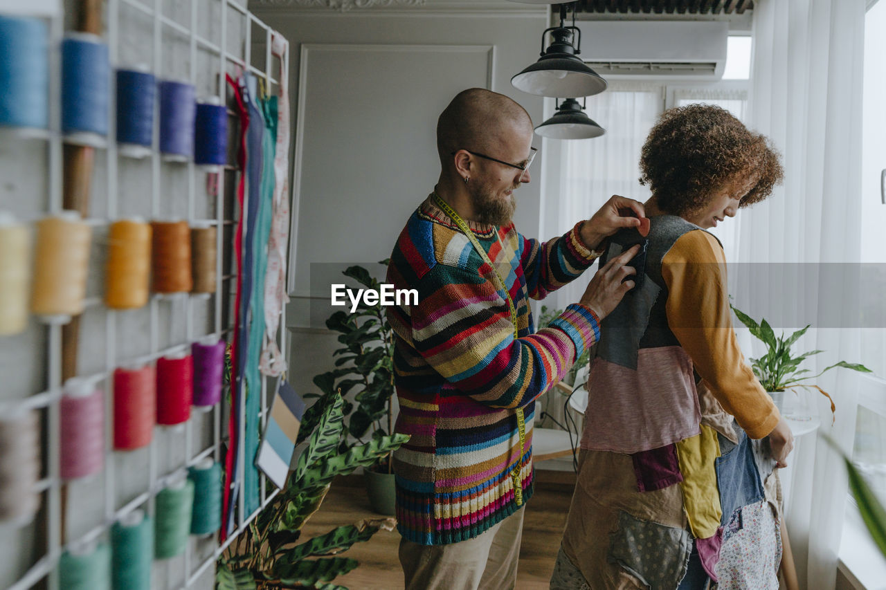 Fashion designer trying patchwork dress on colleague in workshop