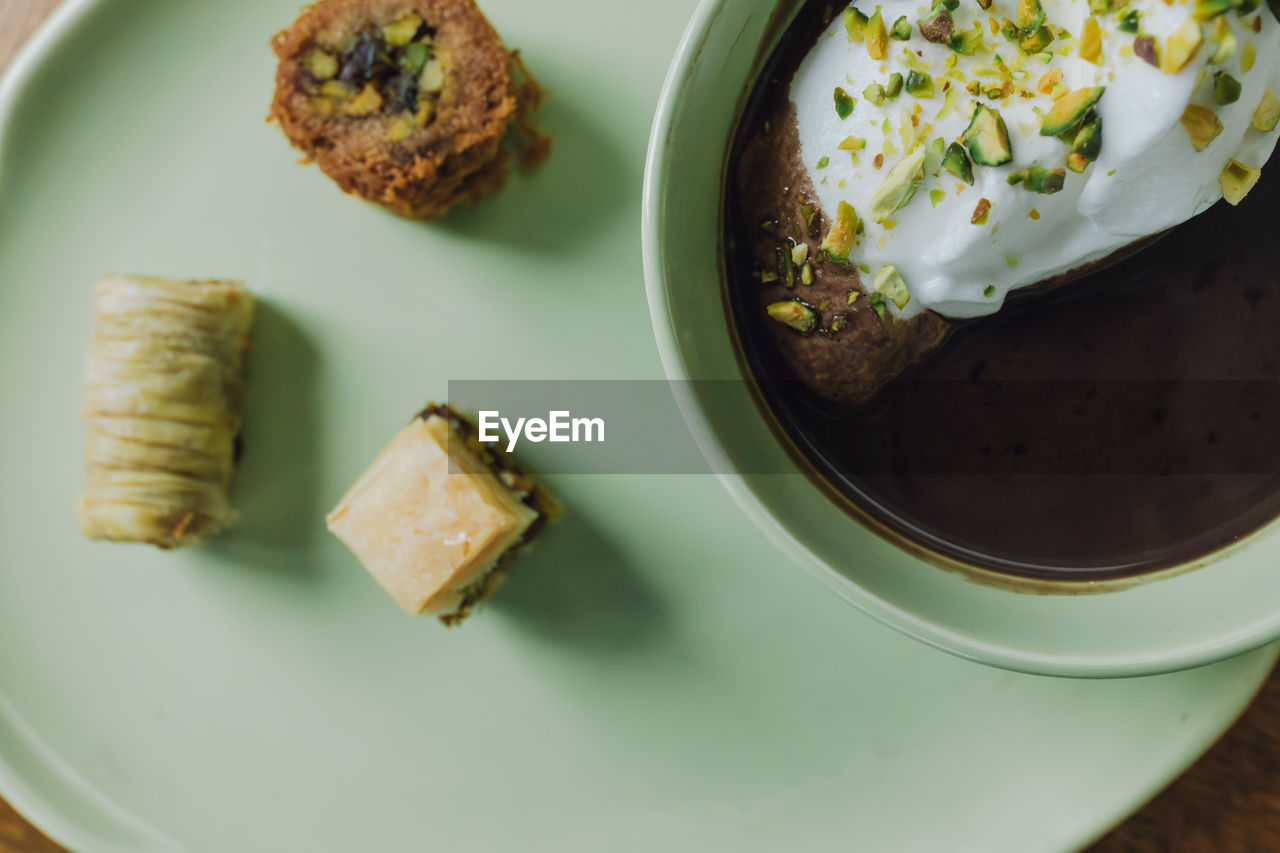 Hot chocolate drink in matching mint green cup and plate with assorted baklava desserts