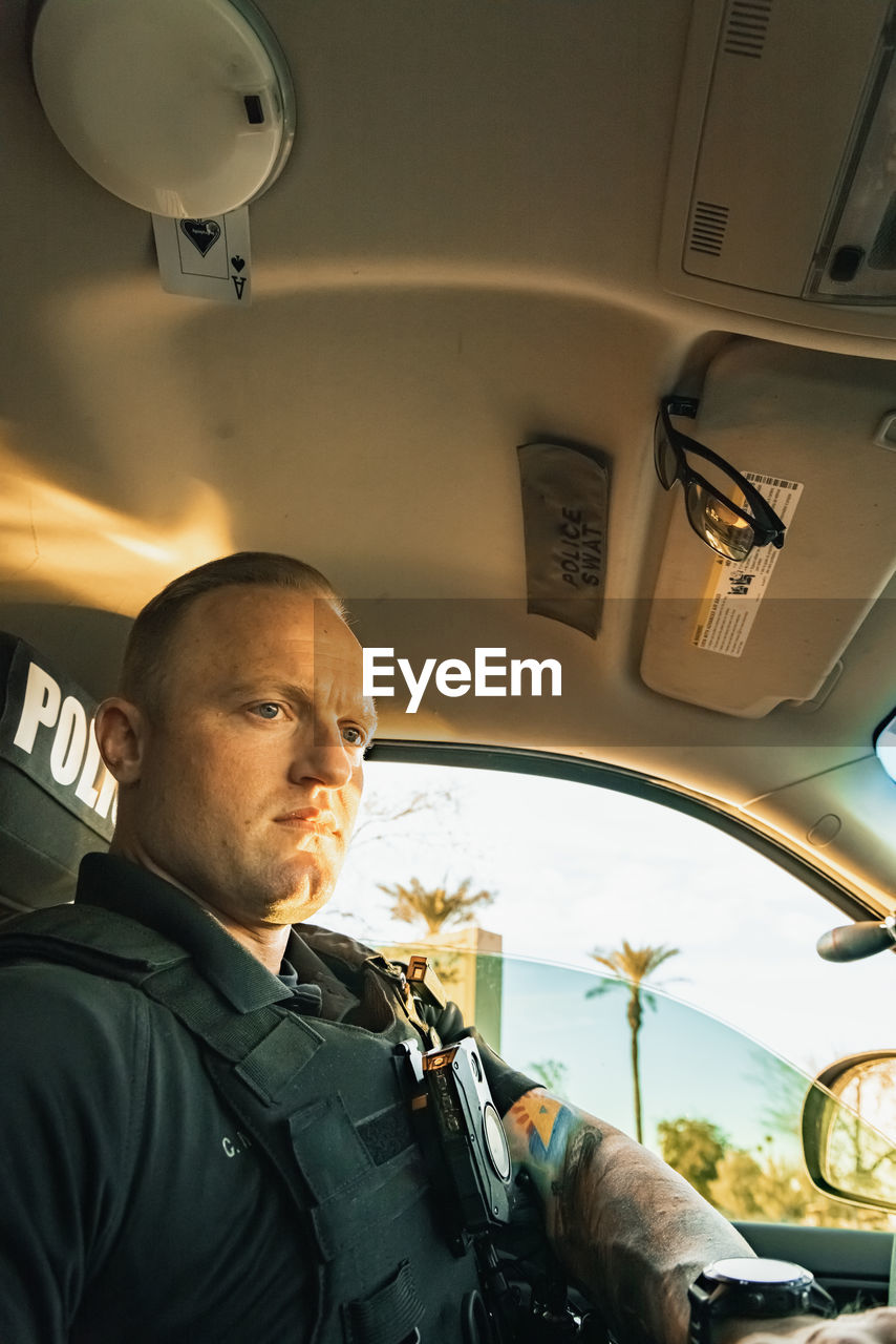 Vertical image low angle shot of of white male caucasian police officer sitting inside a cop vehicle