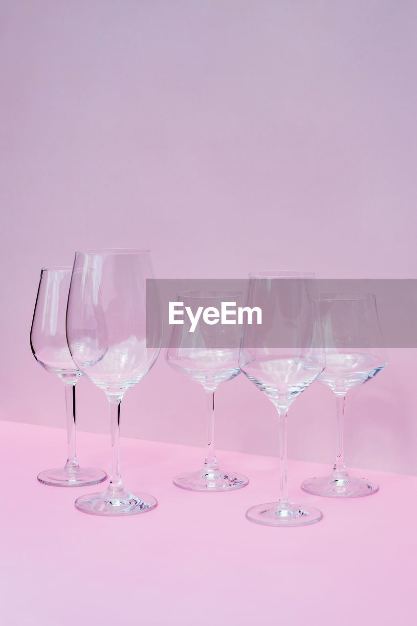 Various empty wine glasses on a pink background with space for text.