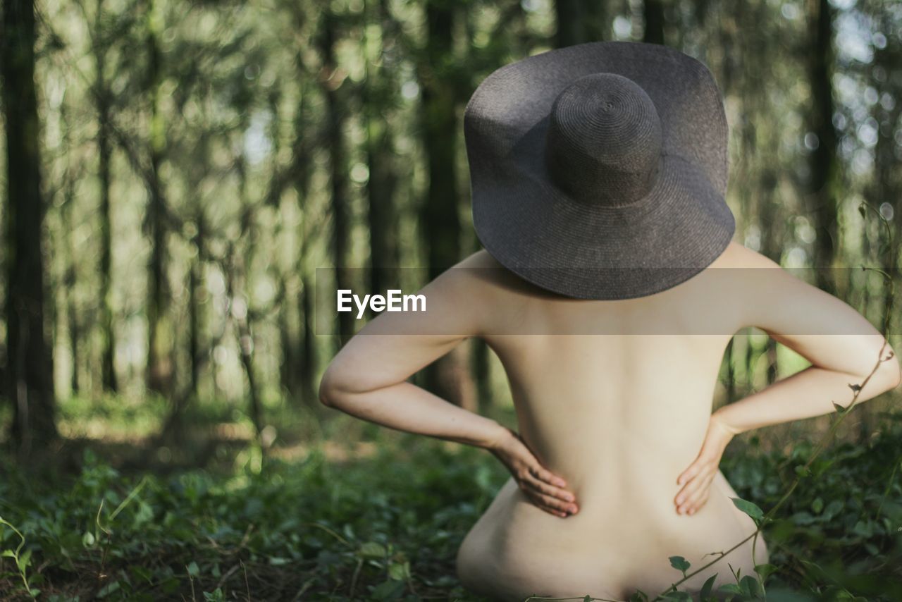 Midsection of naked woman wearing hat while sitting in forest