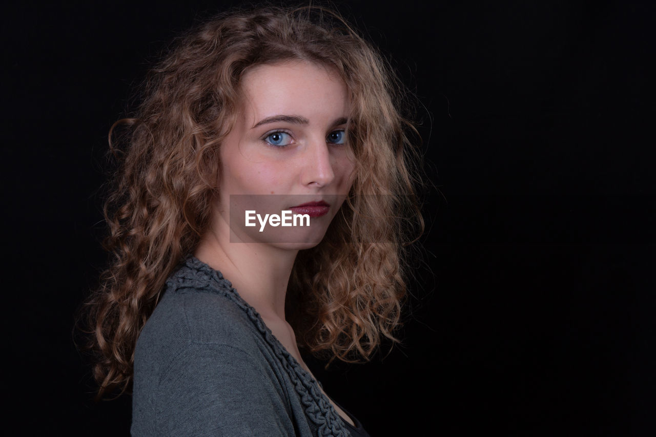 Portrait of beautiful teenage girl against black background