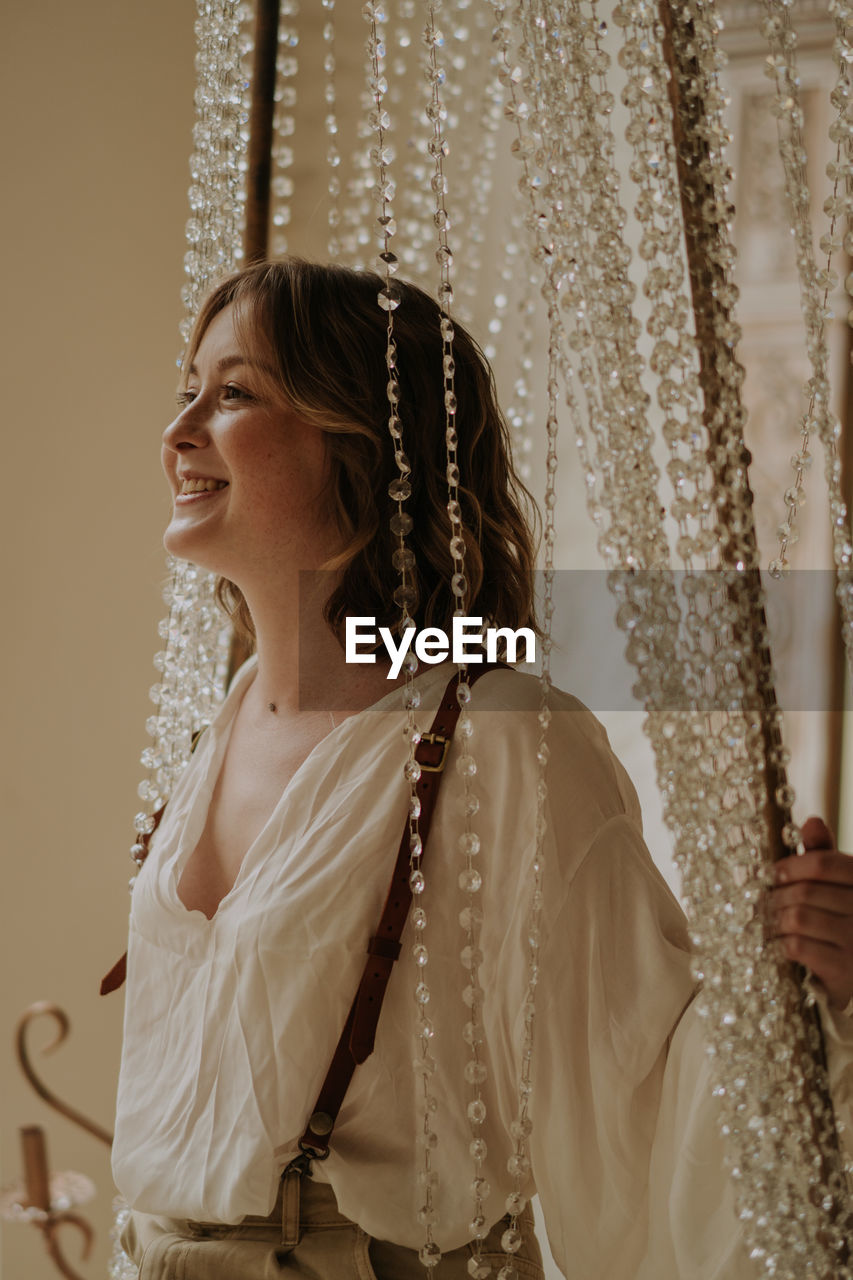 Young female in victorian shirt sitting in giant crystal chandelier and smile