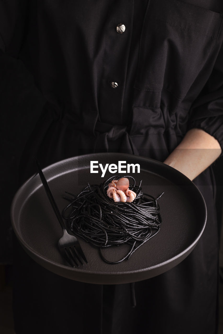 Woman holding a plate with spaghetti with cuttlefish ink and octopus