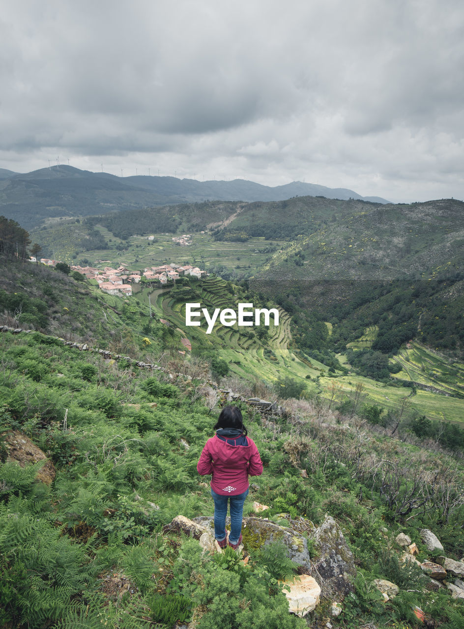 Rear view of woman standing on mountain against cloudy sky