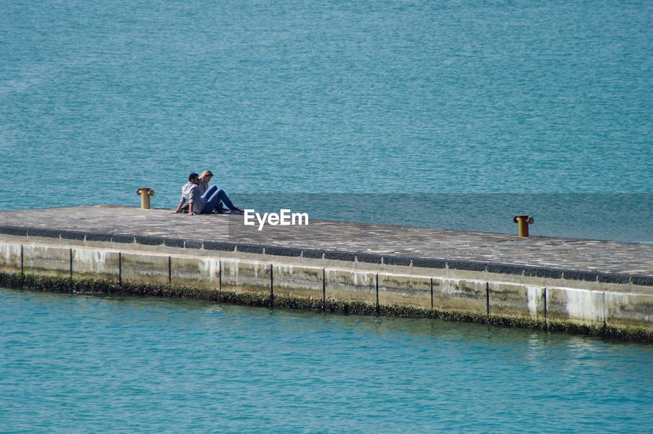 Couple sitting on pier at sea