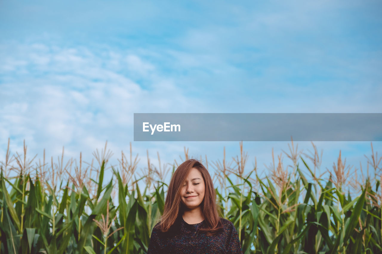 Smiling beautiful woman standing at farm against sky