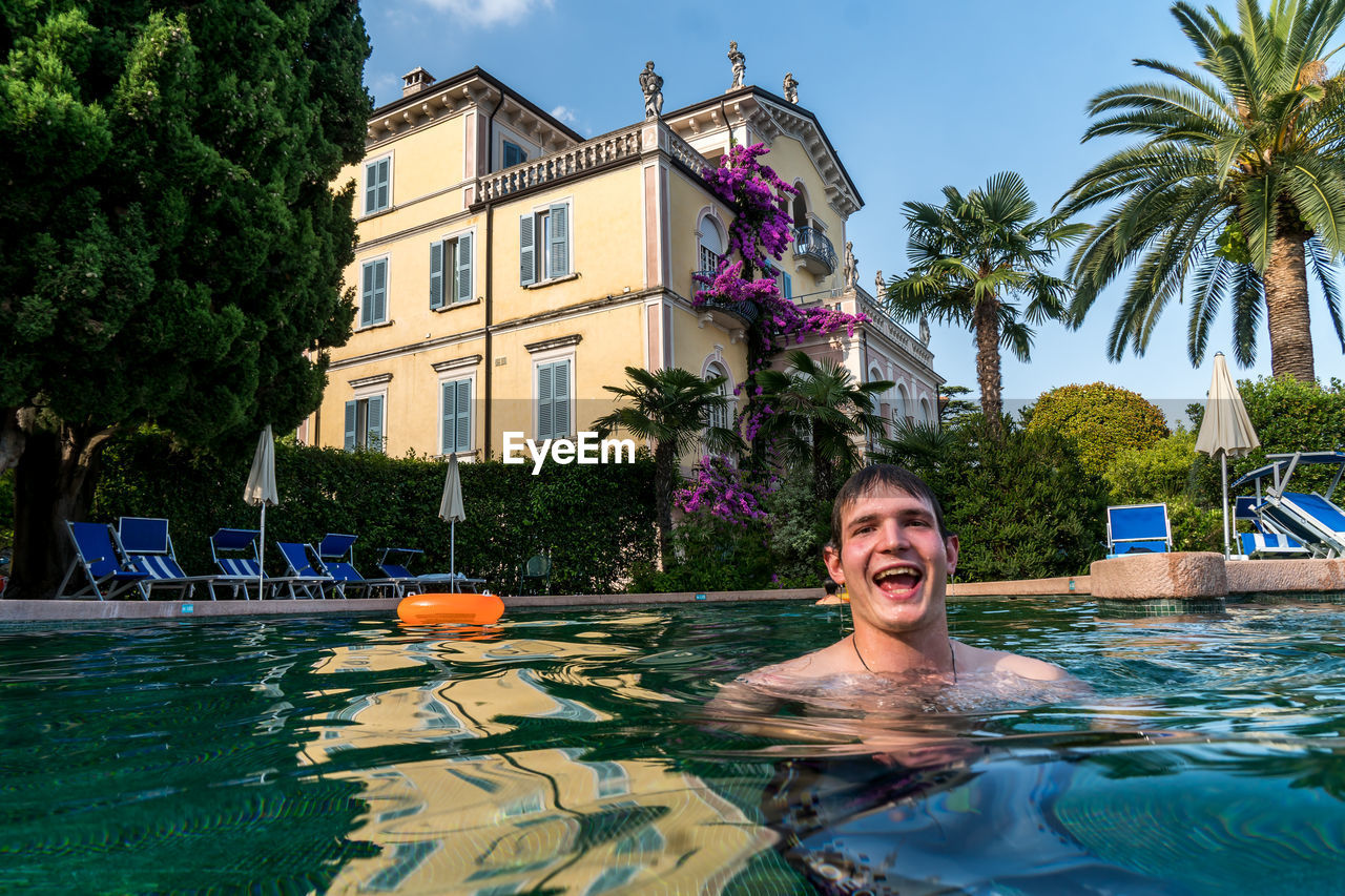 Portrait of smiling man swimming in pool against house