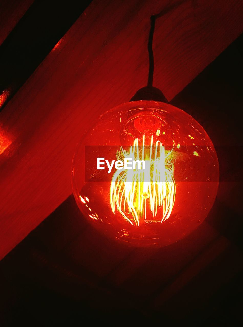 Low angle view of illuminated light bulb hanging from wood