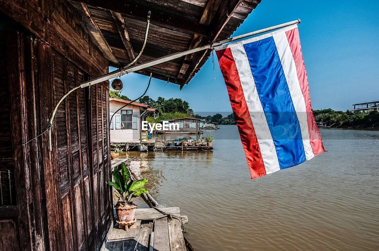 Thai flag on house by river against clear sky