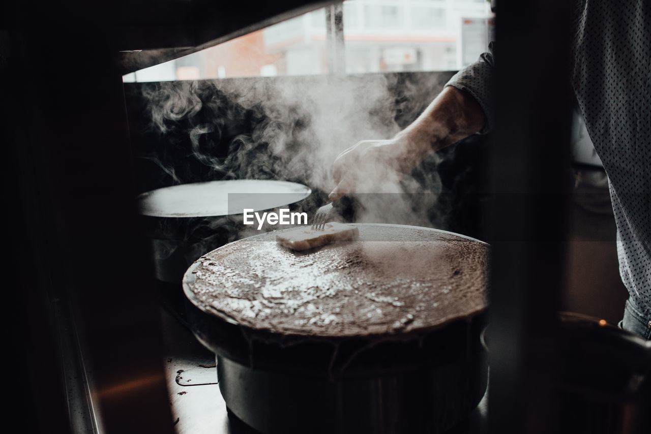 Hand of chef buttering hot crepes while cooking at restaurant kitchen