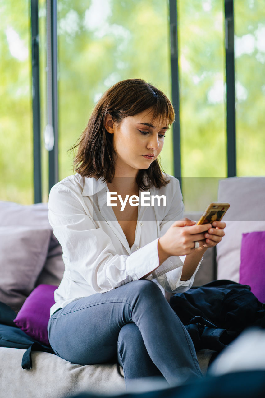 Young woman using mobile phone while sitting on a couch.