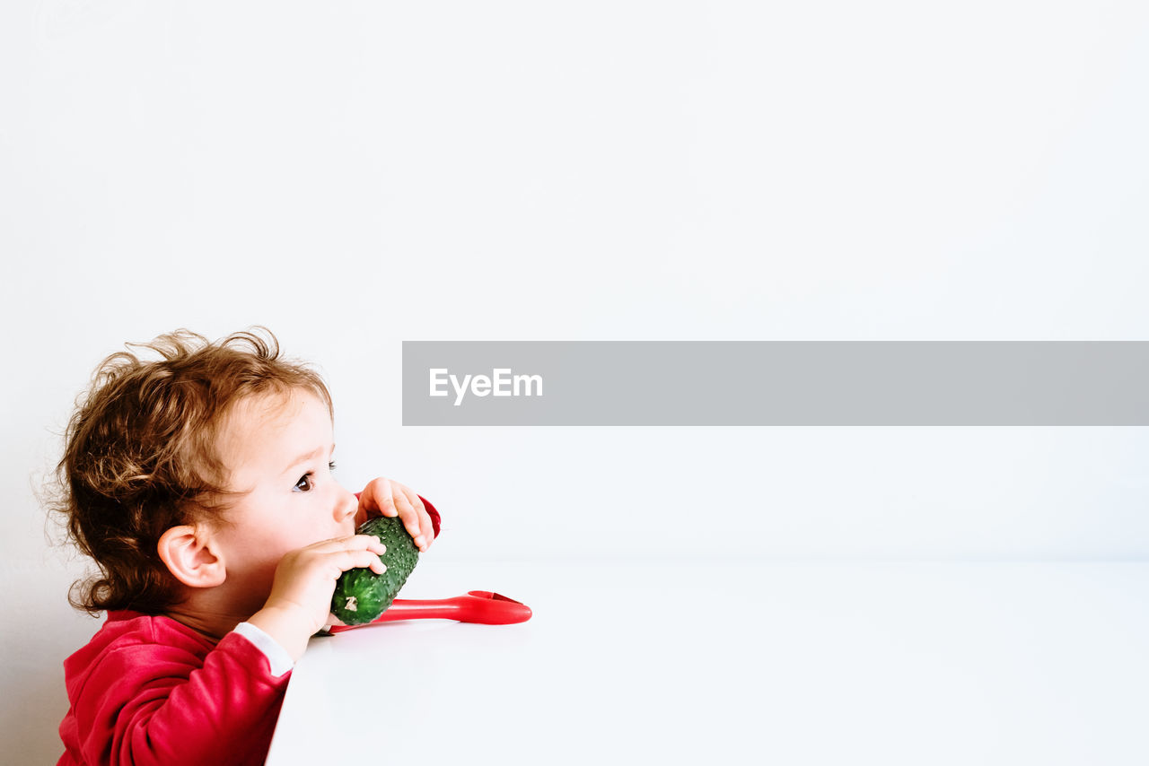 Close-up of cute baby eating food against white background