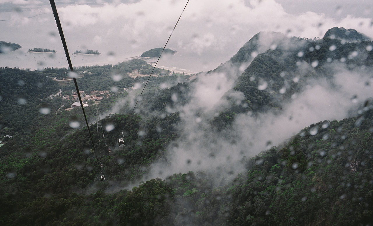 Overhead cable car over mountains seen through wet window