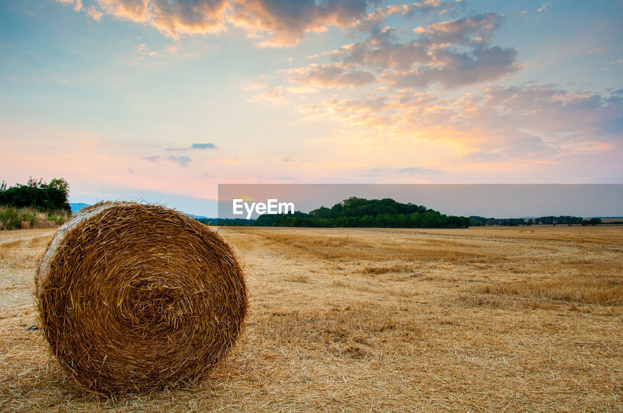 Hay bale on field against sky during sunset