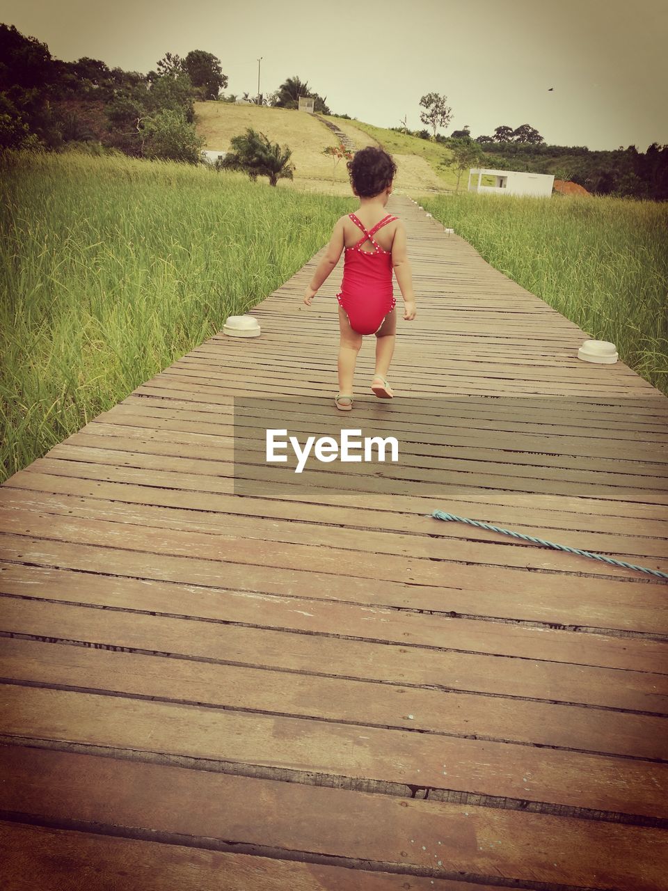 REAR VIEW OF WOMAN WALKING ON FOOTPATH AMIDST GRASS