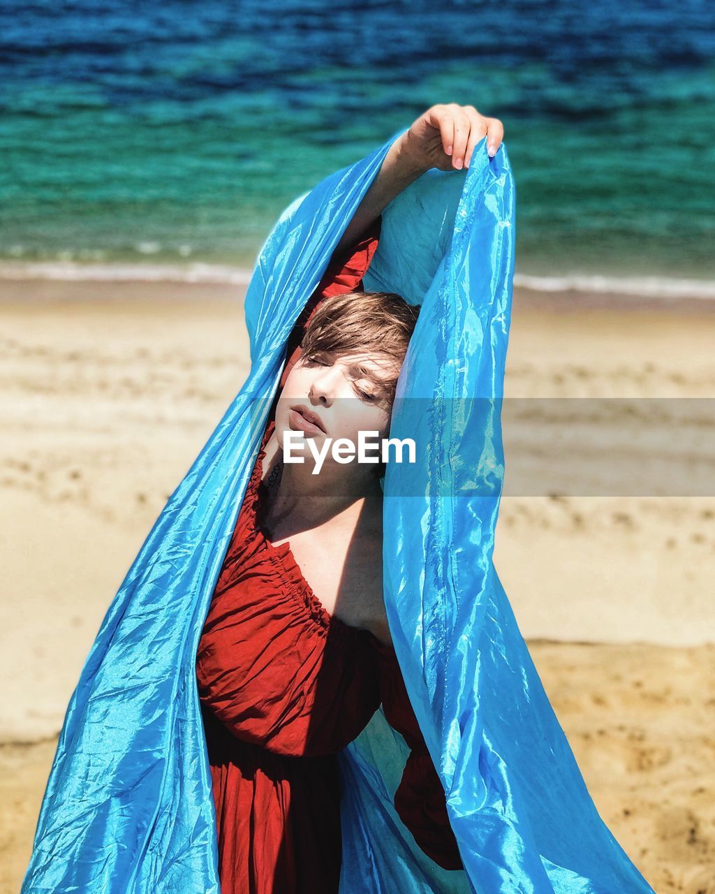 Teenage girl with blue textile standing at beach during summer