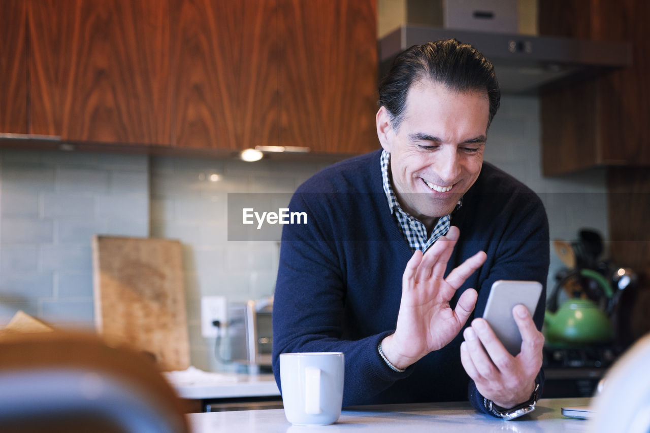 Man waving while looking at smart phone in home