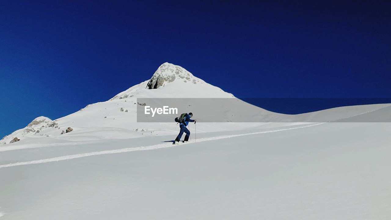 Low angle view of man skiing on snowcapped mountain against clear blue sky