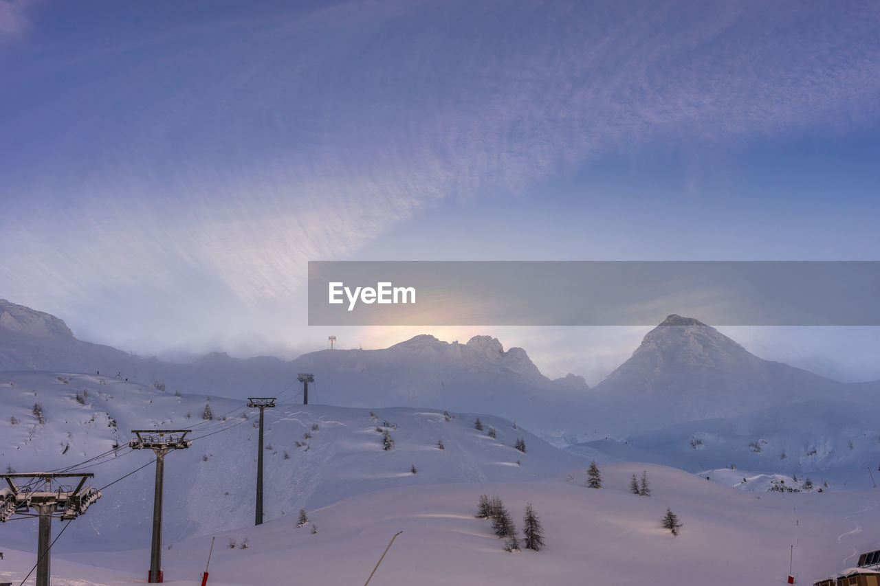 A chairlift running up the mountain, with a rainbow halo over the peak