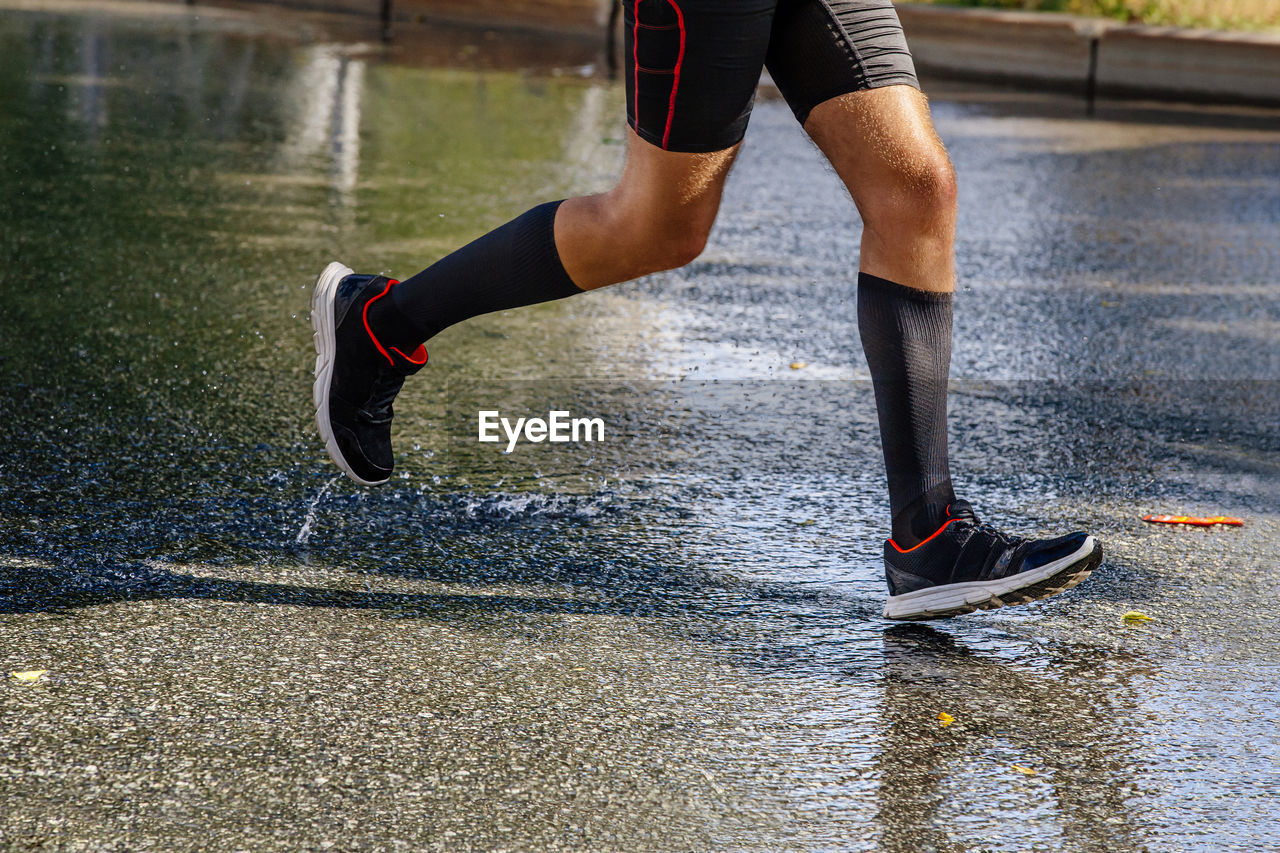 Legs male runner in compression socks running on wet asphalt