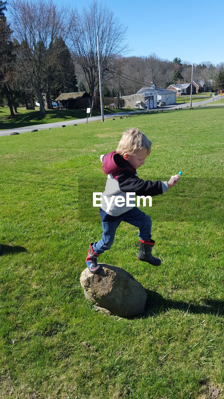 Boy jumping from rock on grassy field at park