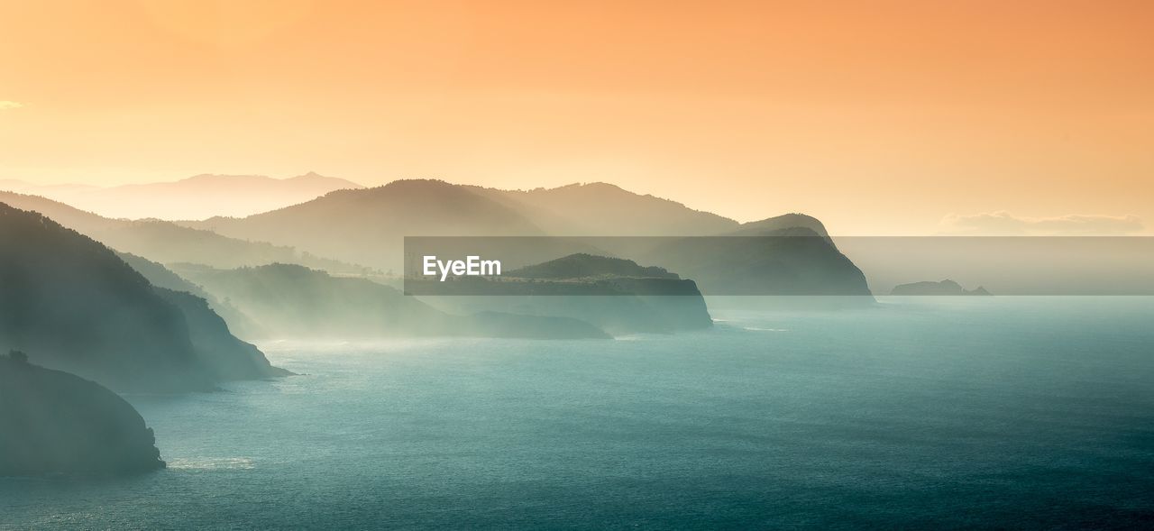 Scenic view of sea and mountains against sky during sunset