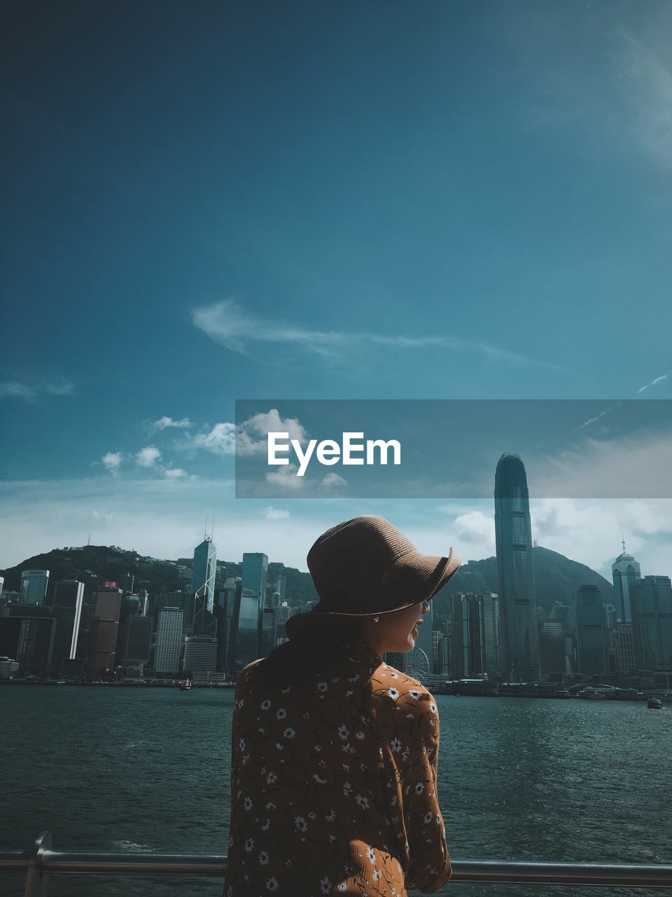 Rear view of woman standing by sea against buildings in city