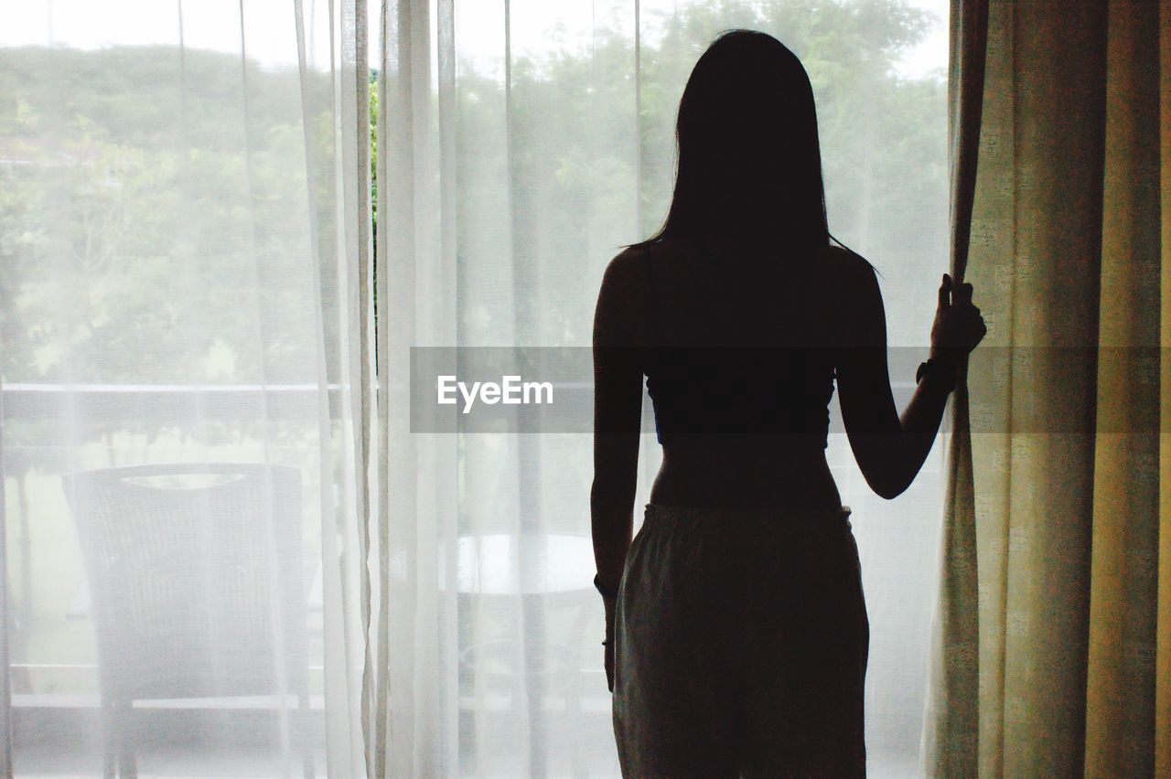 Rear view of silhouette woman standing against curtain