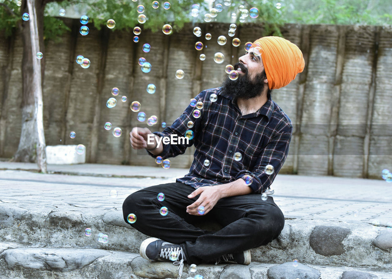 Full length of man wearing turban sitting by bubbles