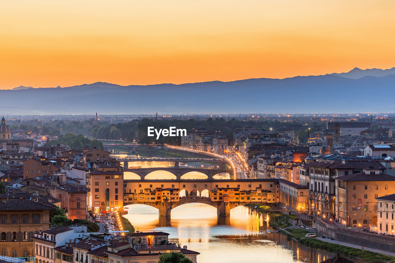 High angle view of ponte vecchio over river amidst buildings against sky during sunrise
