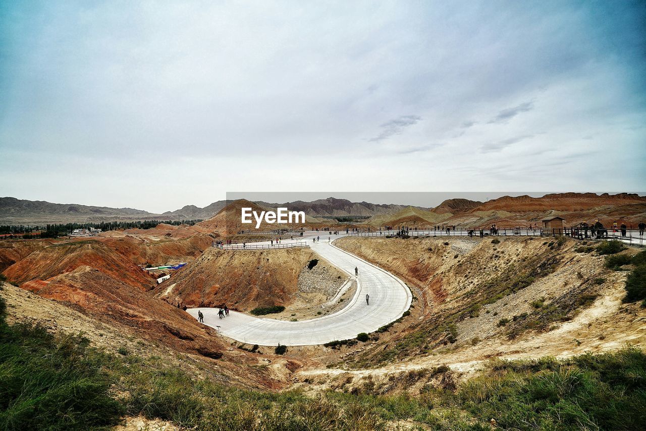 People on road in dramatic landscape against sky at zhangye danxia national geological park