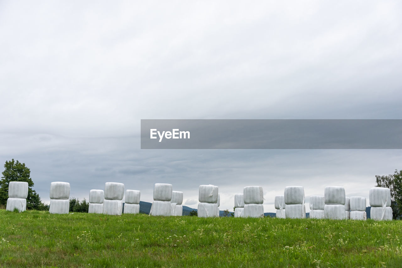 cemetery, grass, plant, sky, cloud, nature, in a row, environment, no people, grave, architecture, day, stone, tombstone, white, field, landscape, land, outdoors, green, memorial, horizon, copy space, pasture, rural area, large group of objects, meadow, overcast, grassland, death, built structure, beauty in nature, hill