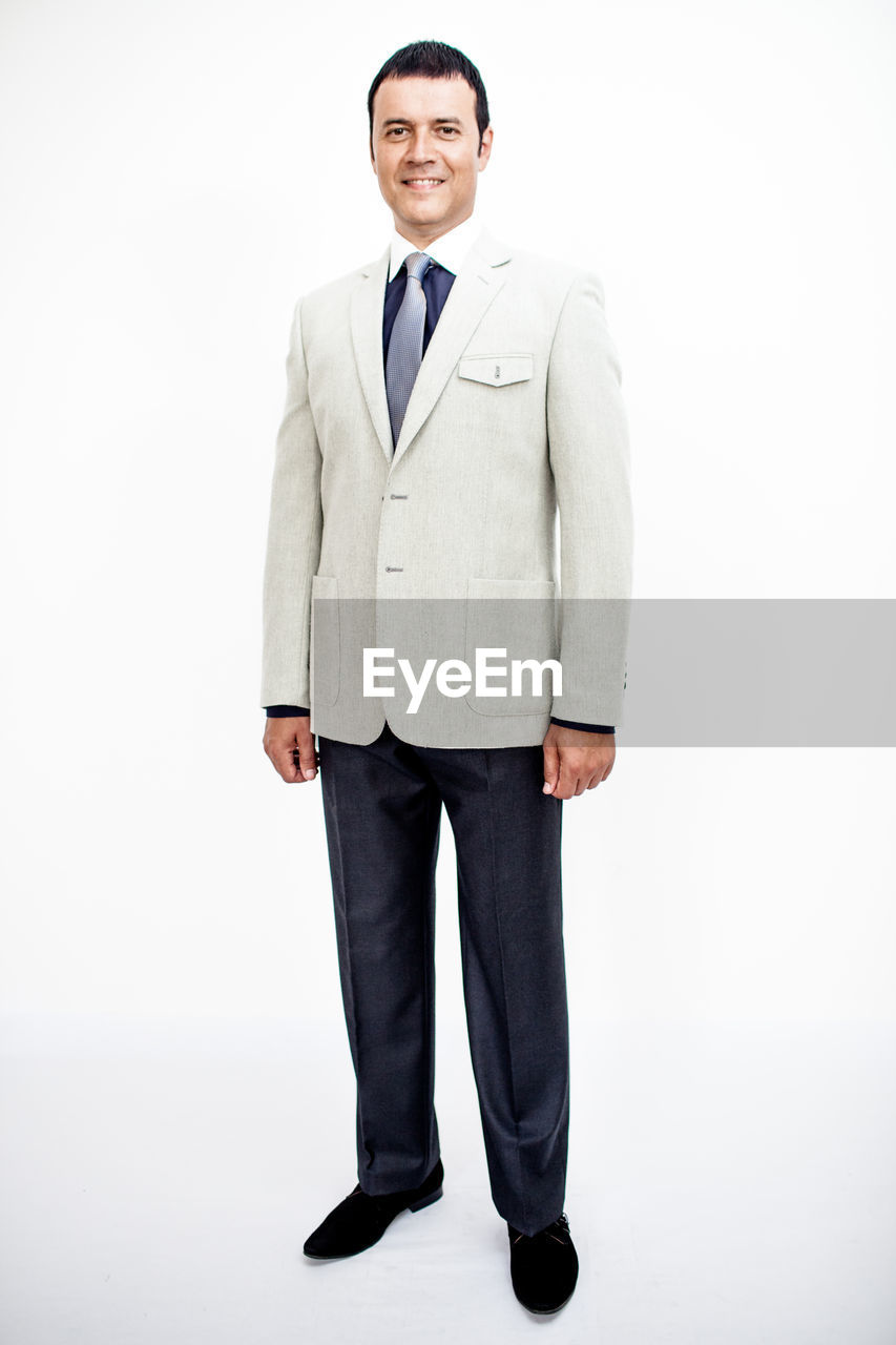 Portrait of confident smiling businessman wearing suit standing against white background