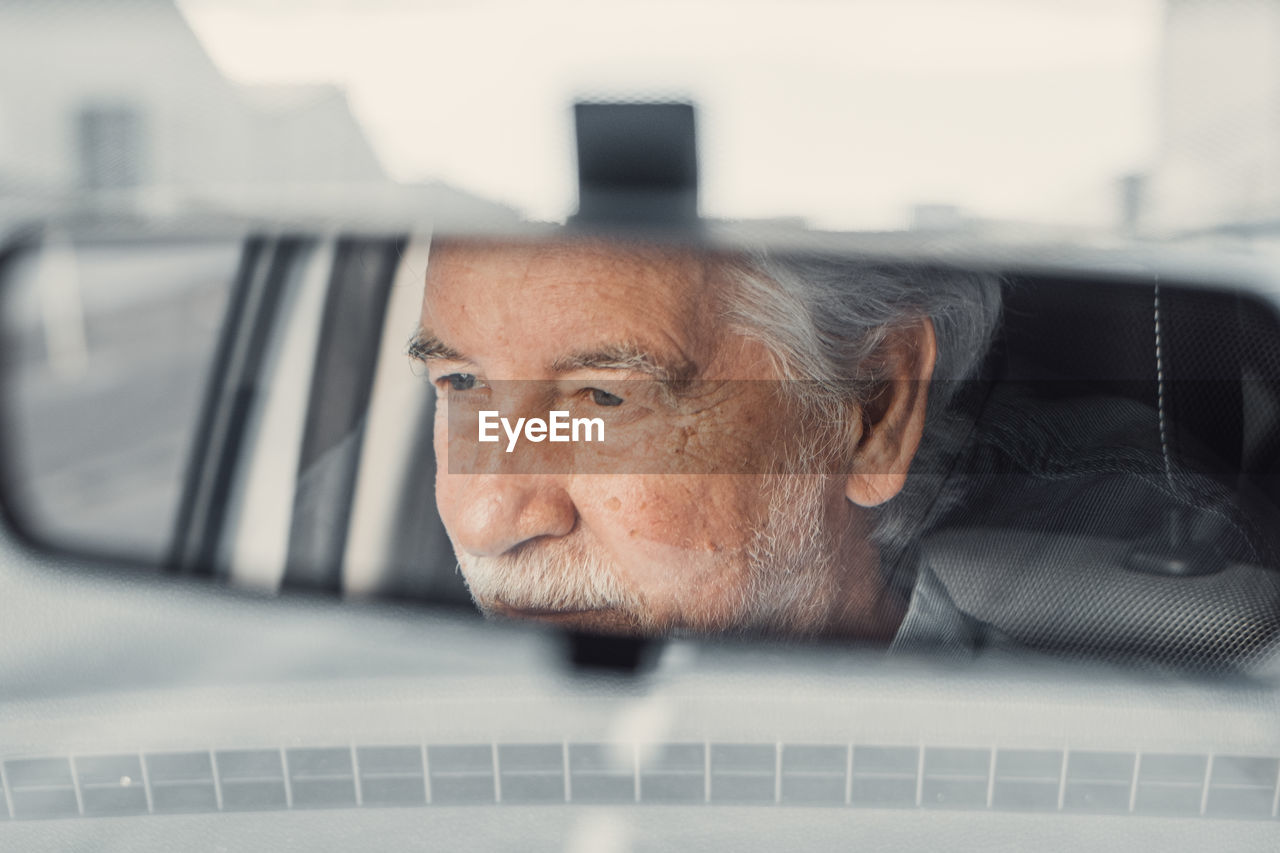 Reflection of smiling senior man sitting in car