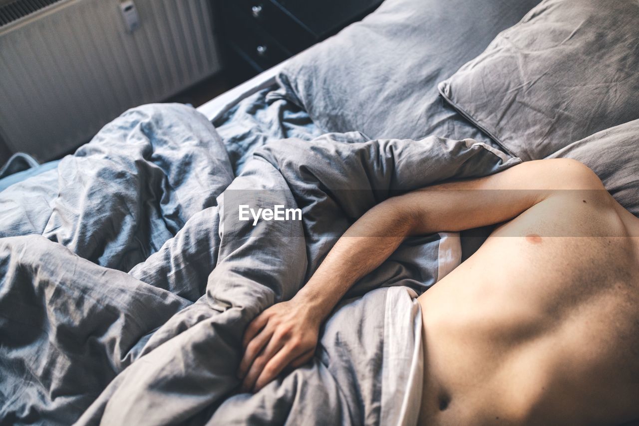 Midsection of shirtless man lying on bed at home