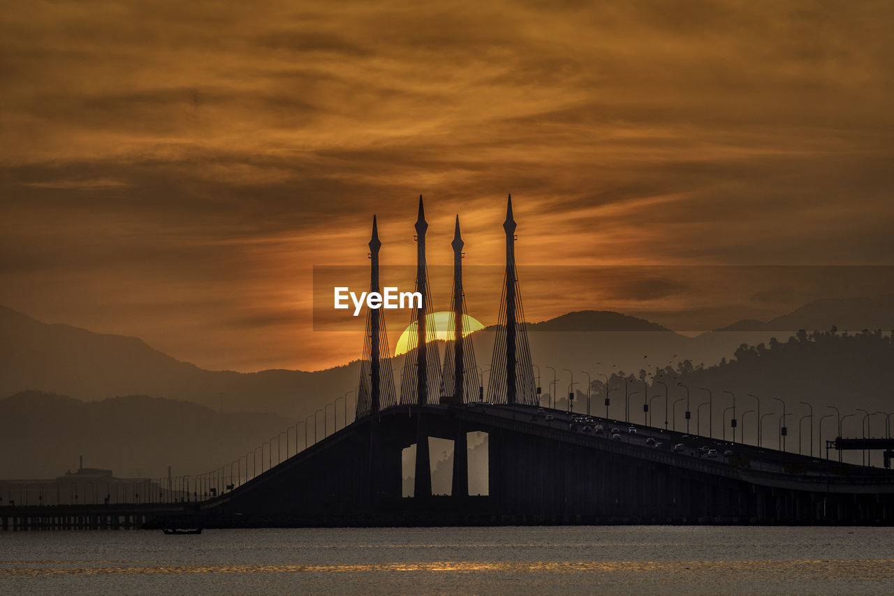 Silhouette penang bridge over sea against sky during sunset