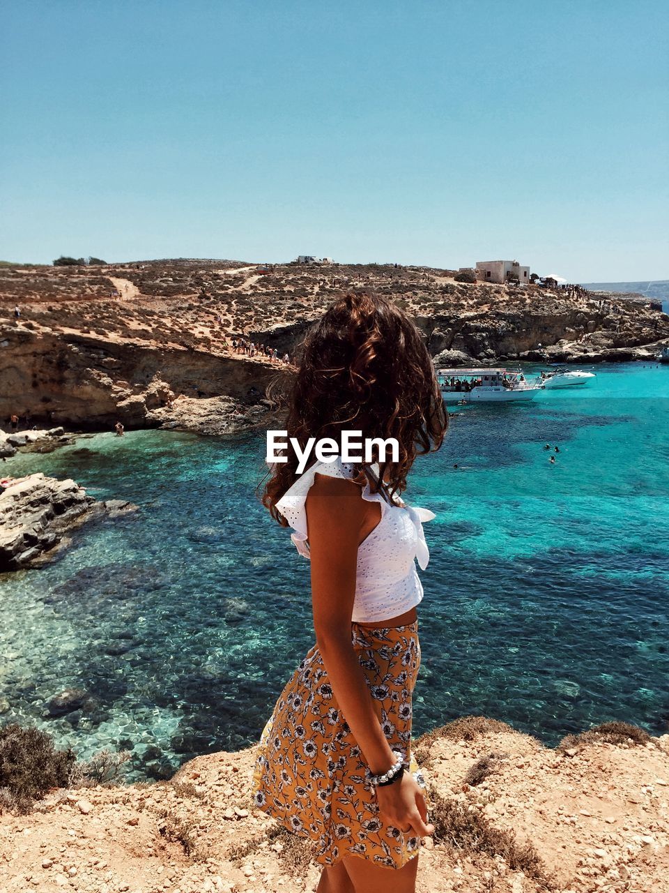 Woman looking away while standing on rock by sea against sky