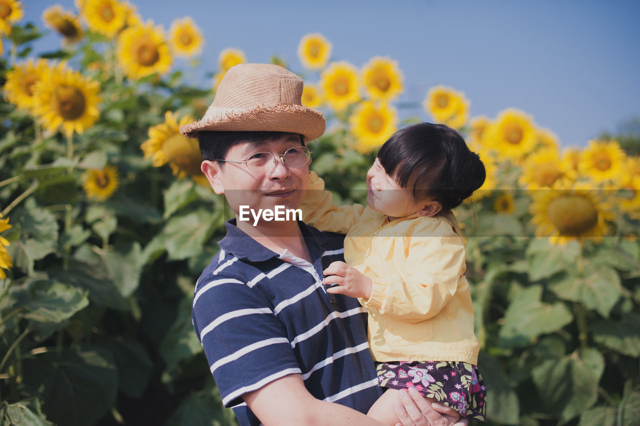 Man holding daughter against sunflowers