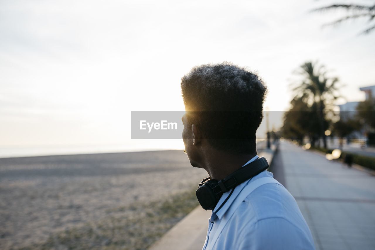 Afro man with headphones looking at view from beach during sunset
