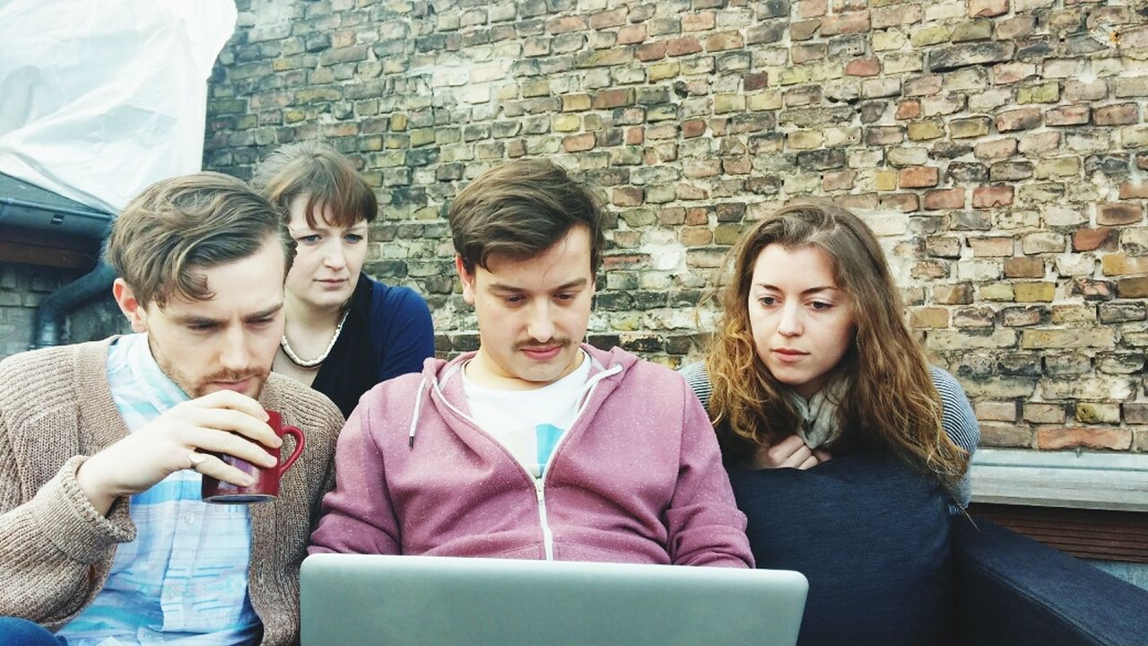Friends watching movie on laptop against brick wall