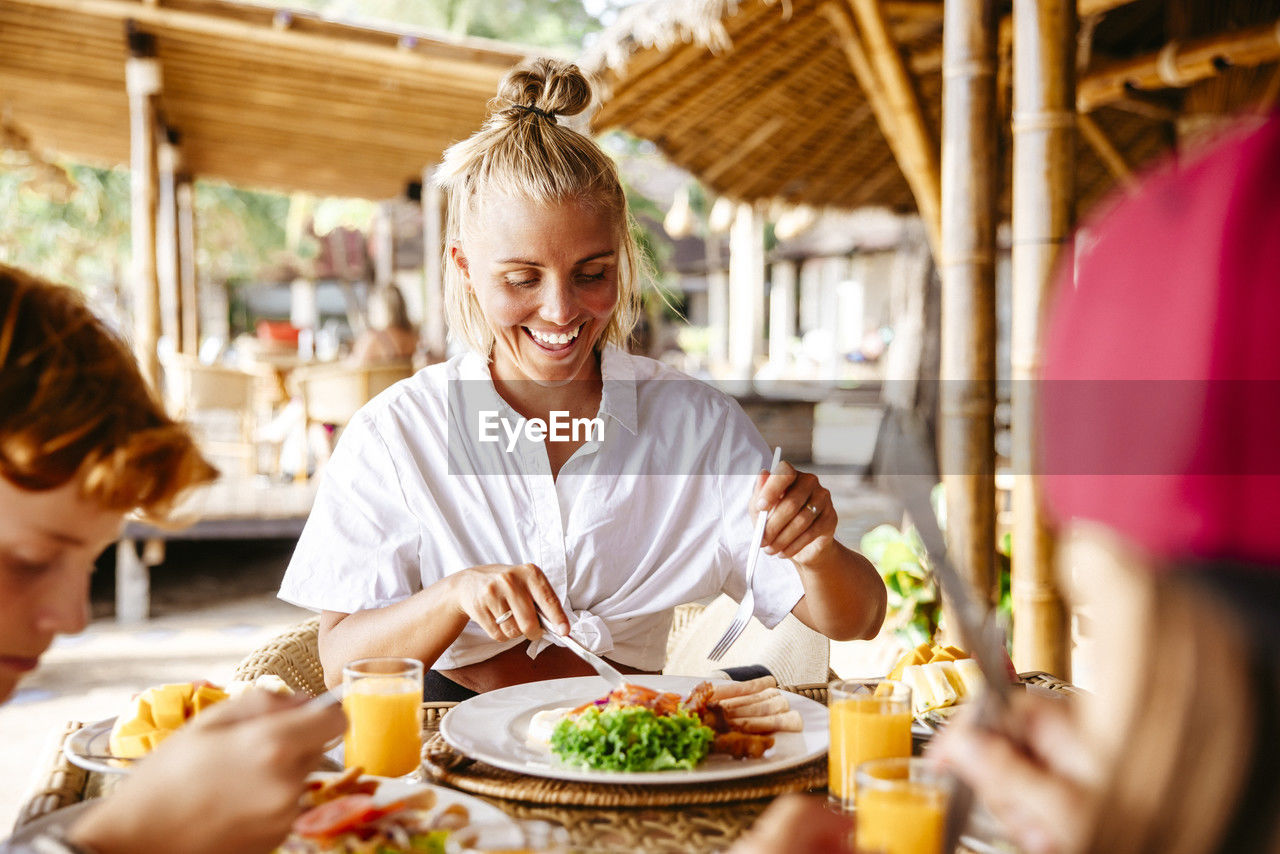 Smiling woman having breakfast with son at table in tourist resort during vacation