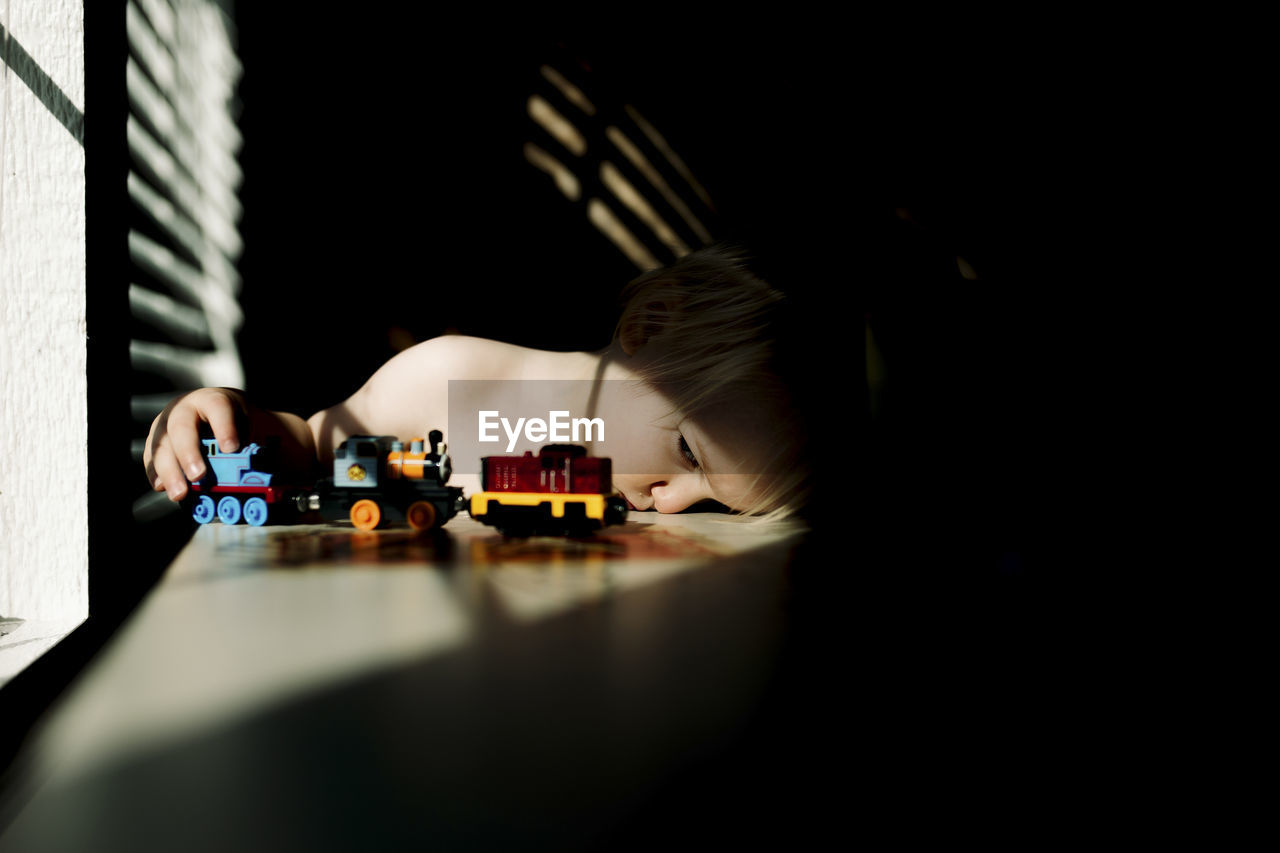 Boy playing with toy train while sitting at table by window